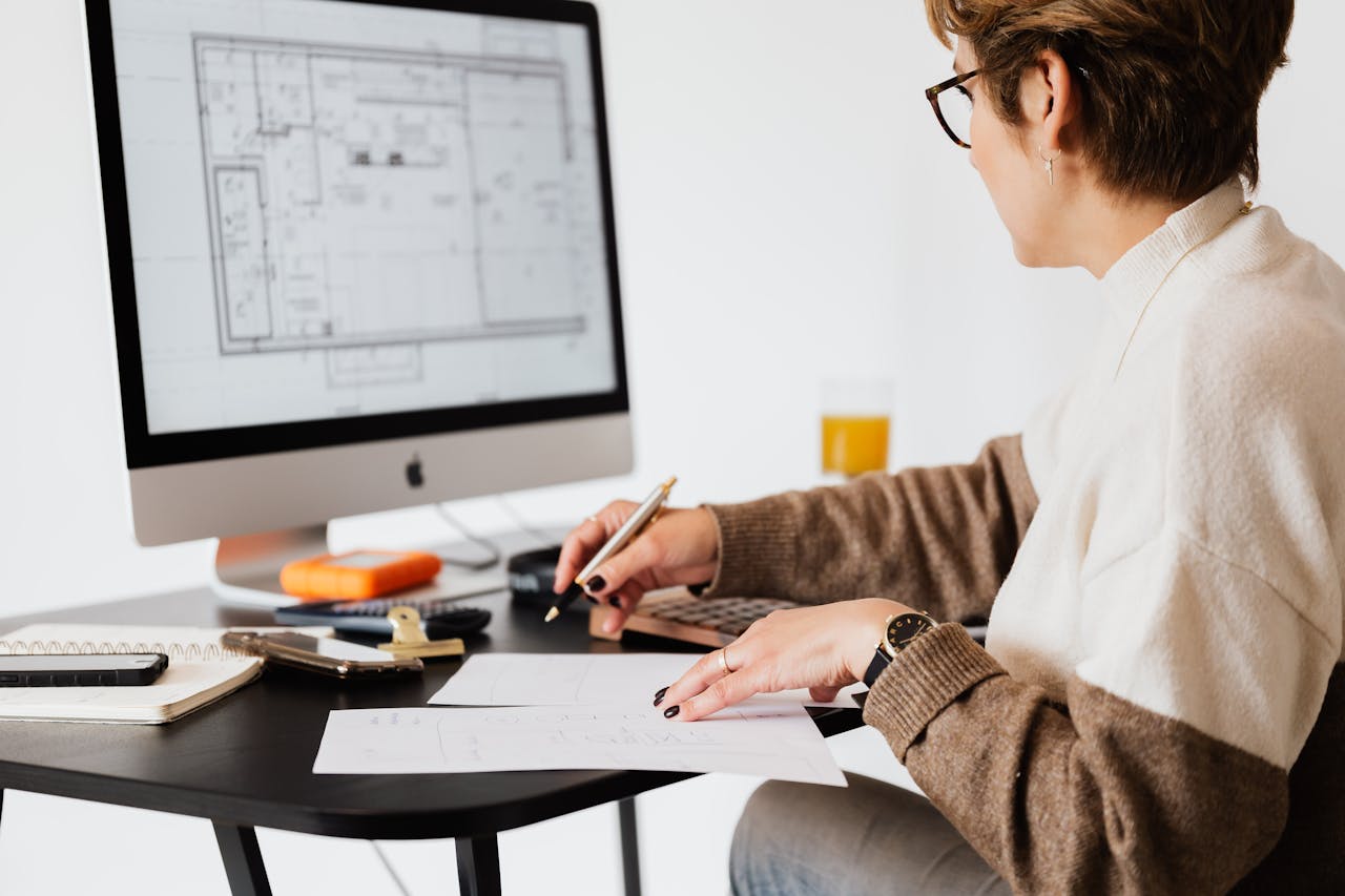 digital Woman designing architectural blueprints using desktop computer in a modern office setting.